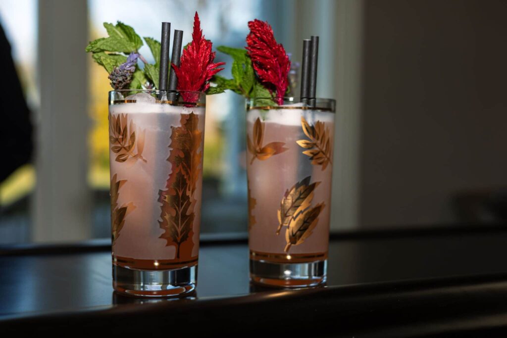 Cocktails in tall glasses garnished with red edible flowers on a bar