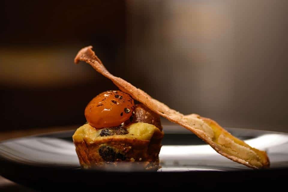 Single canapé with roasted tomato and a crisp shard on a dark plate