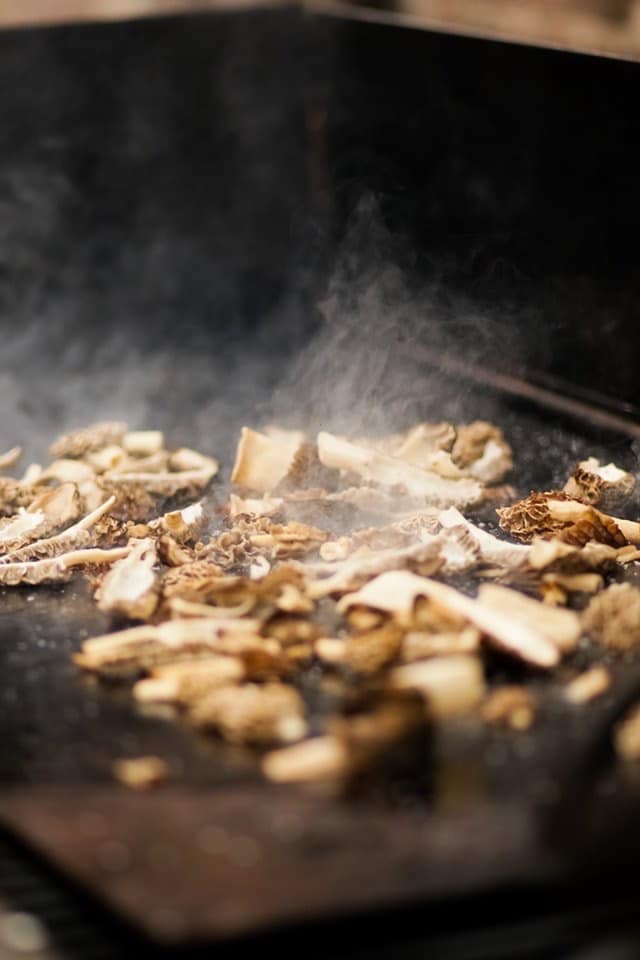 Meat and vegetables cooking on a flat-top grill with steam rising