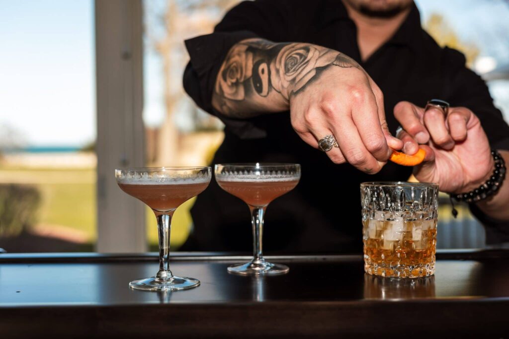 Bartender garnishing cocktails at an outdoor bar overlooking the water