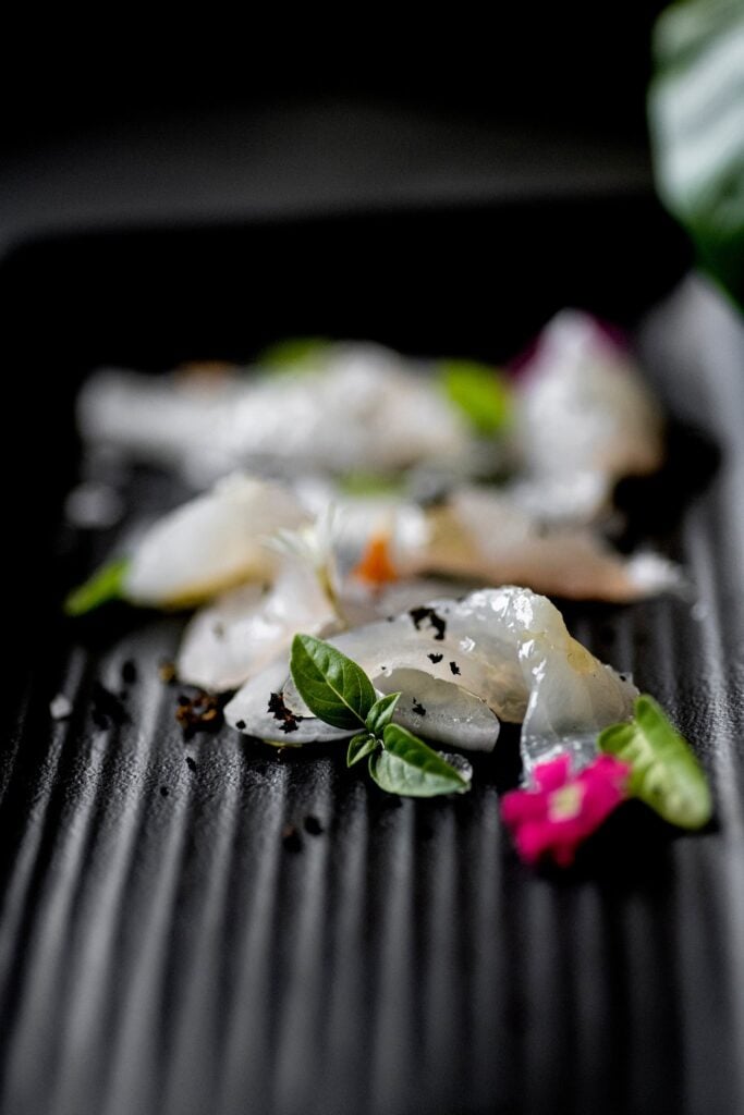 Crudo with edible flowers plated on a dark surface