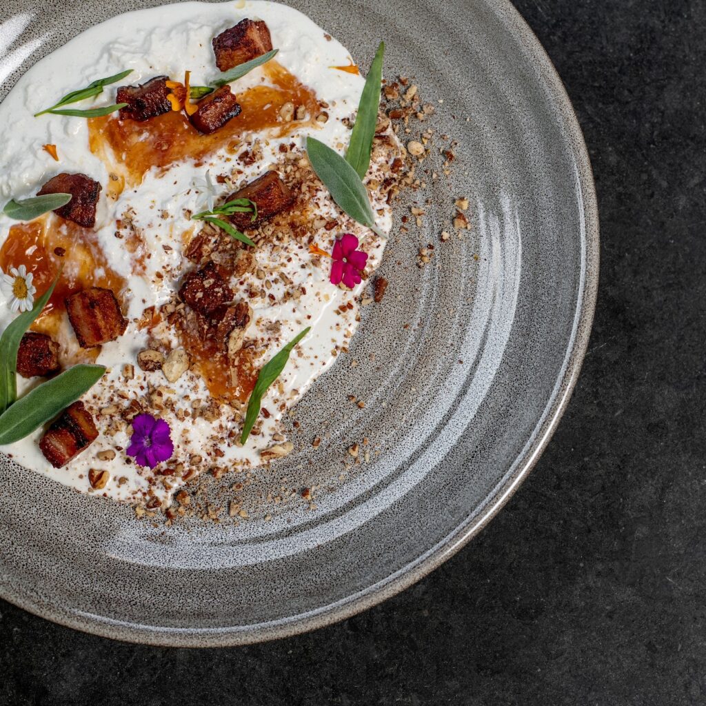 Overhead plated course with pork belly, herbs and edible flowers on a grey plate