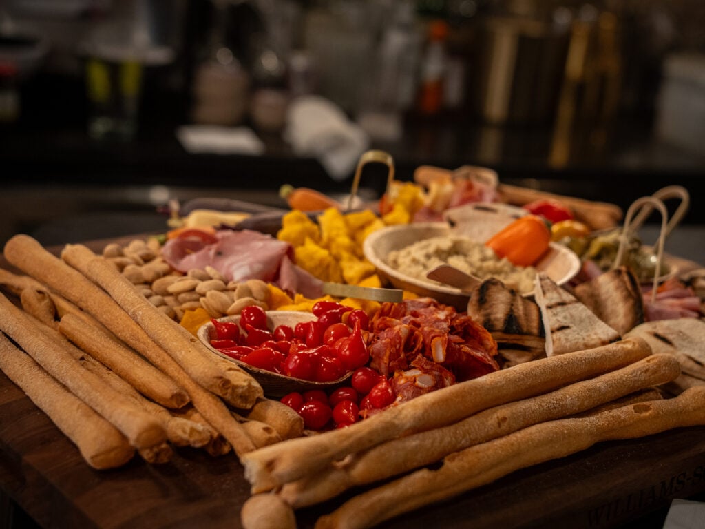 Grazing board with breadsticks, cured meats, roasted peppers, olives and dips