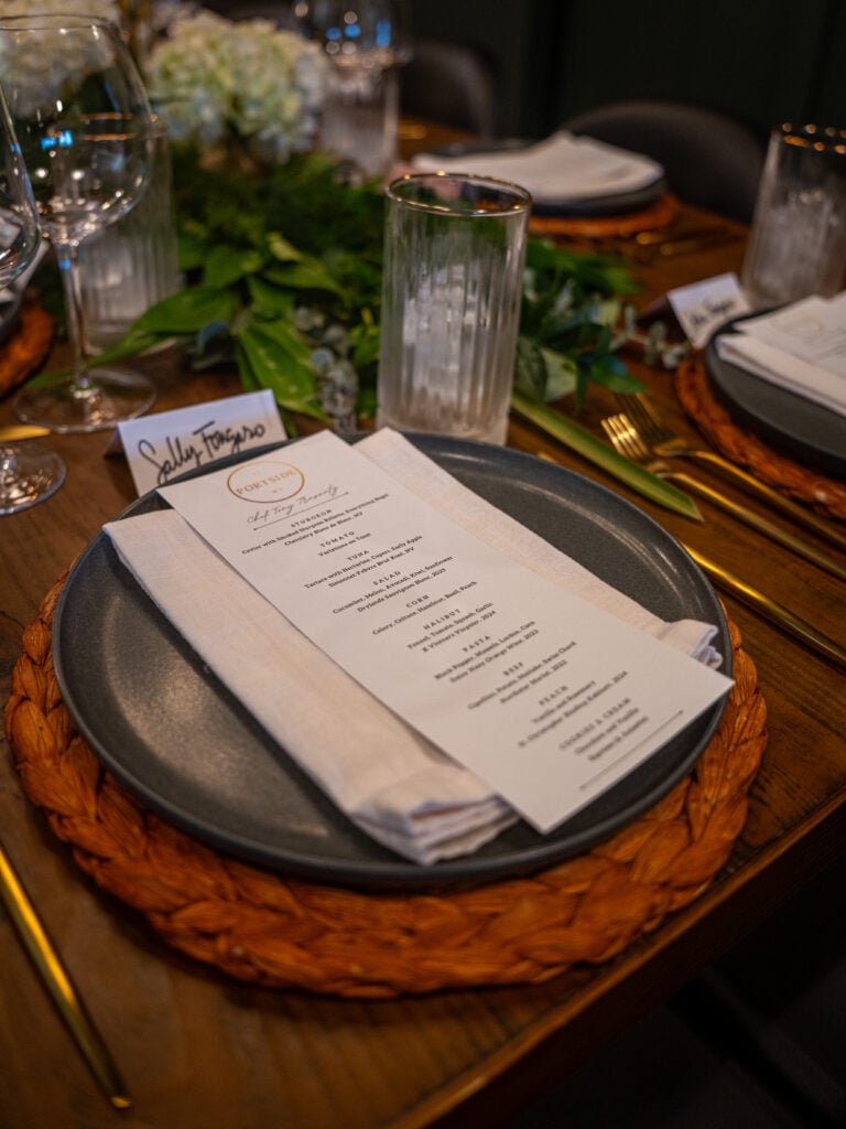Place setting with a printed menu card, greenery and glassware