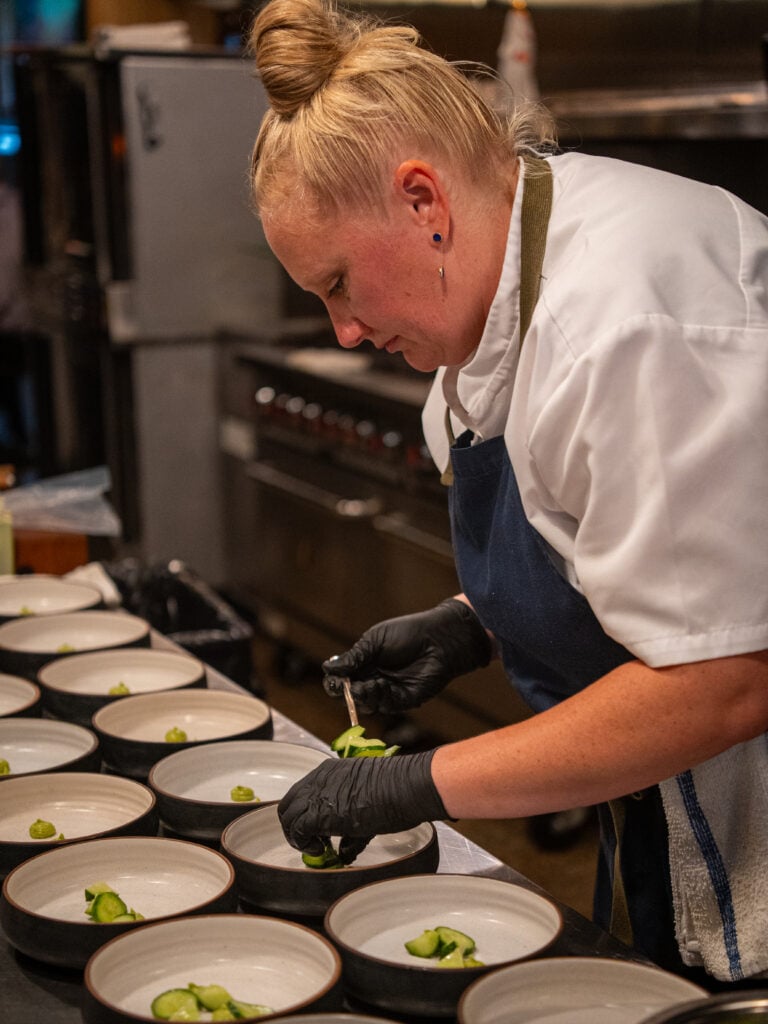 Chef plating a course into shallow bowls in the kitchen