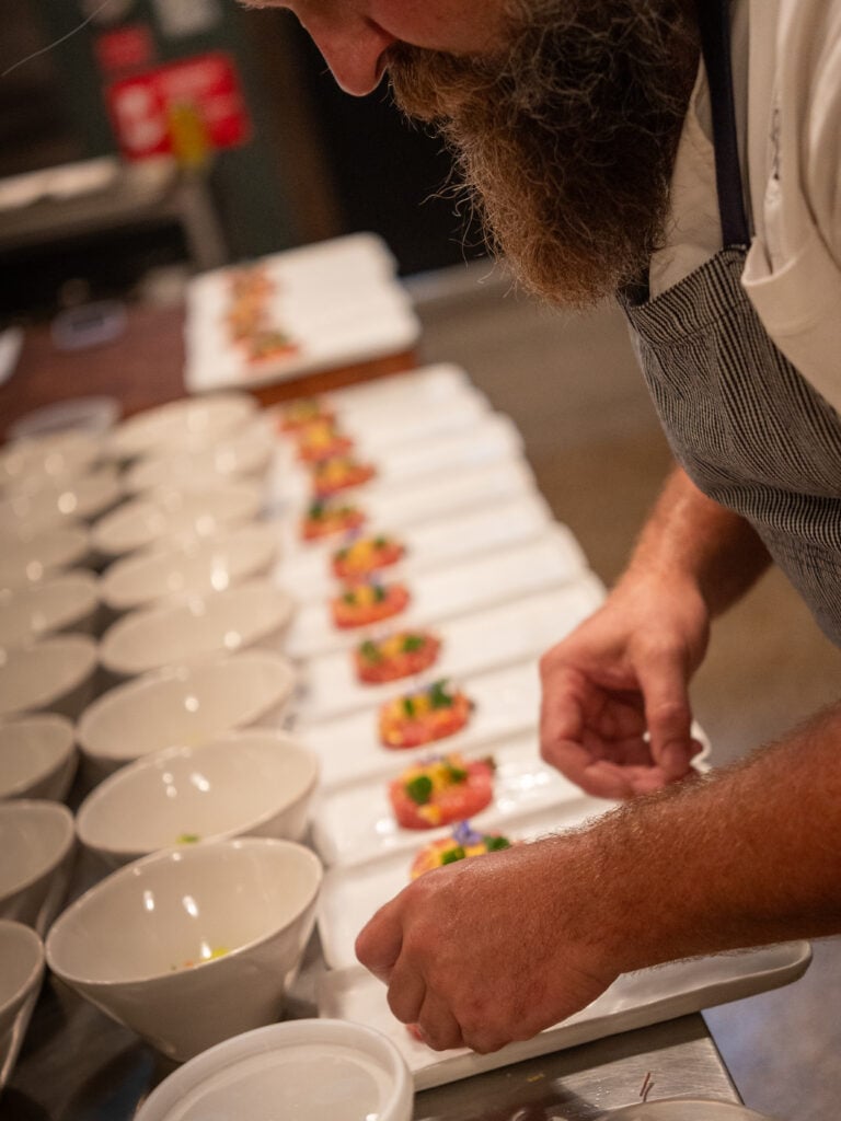 Chef finishing a row of canapes on rectangular plates
