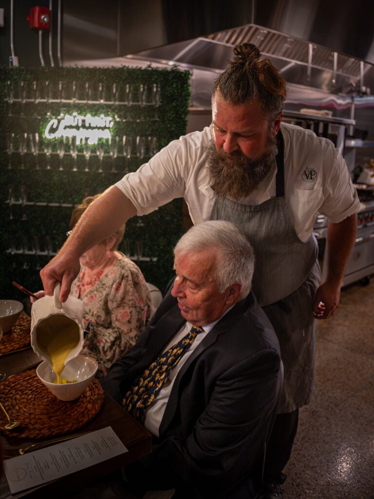 Chef pouring soup at the table for a seated guest