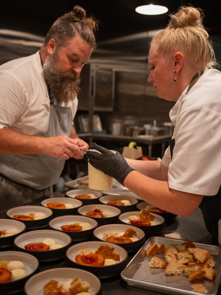 Two chefs plating a course together in the kitchen